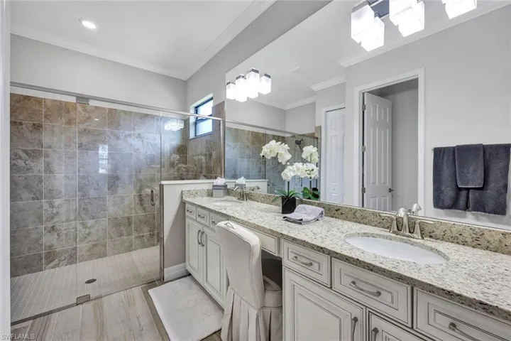 Bathroom featuring dual bowl vanity, ornamental molding, and a shower with shower door