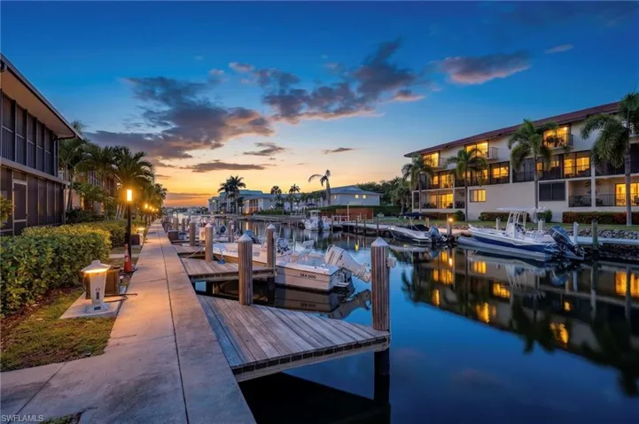 Waterfront property featuring multiple boat slips, a concrete walkway, established landscaping, and palm trees