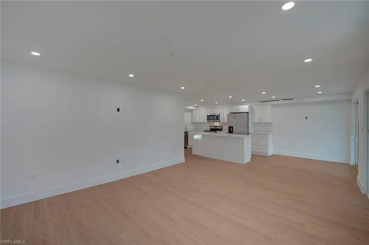 Open-concept living area with wood-finish flooring, recessed lighting, and white baseboards