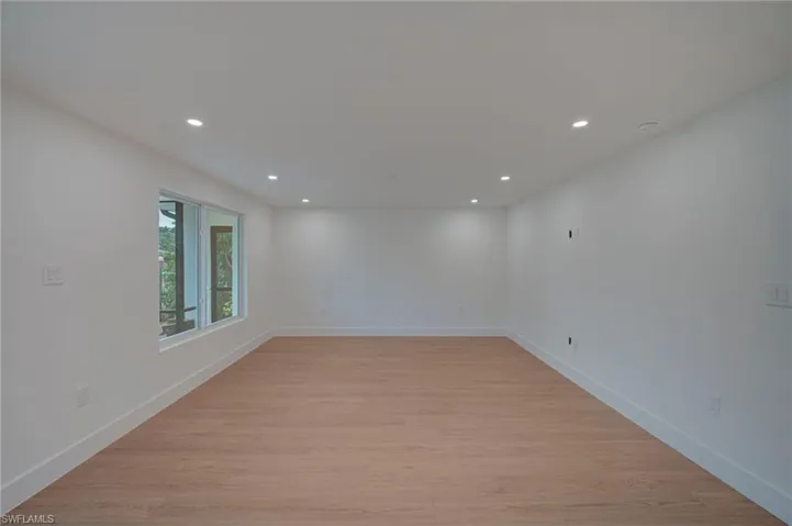 Spacious room featuring wood-finish flooring, recessed lighting, and white baseboards