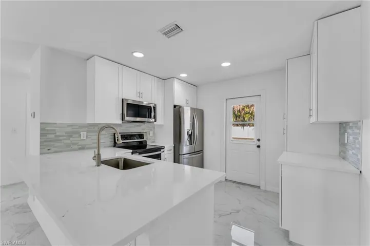 Kitchen featuring white cabinets, stainless steel appliances, recessed lighting, light stone counters, and light marble finish floors