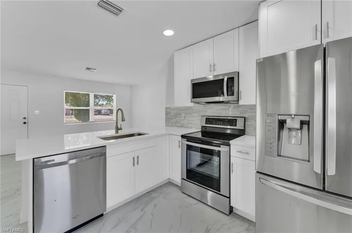 Kitchen with stainless steel appliances, light marble finish floors, white cabinets, recessed lighting, and a peninsula