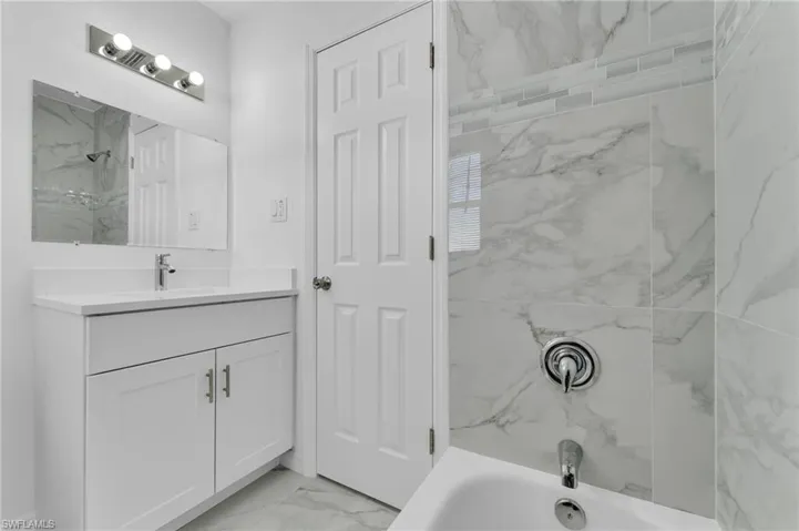 Full bathroom with vanity, light marble finish flooring, and a combined bath / shower with marble appearance