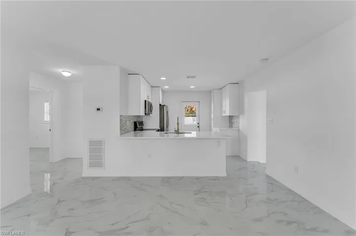 Kitchen with white cabinets, a peninsula, stainless steel appliances, recessed lighting, and backsplash
