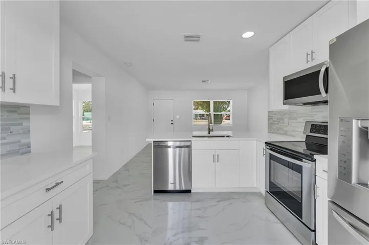 Kitchen featuring tasteful backsplash, stainless steel appliances, a peninsula, white cabinetry, and recessed lighting