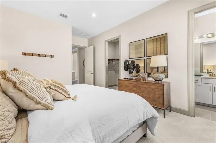 Bedroom with ensuite bathroom, a walk in closet, and light colored carpet