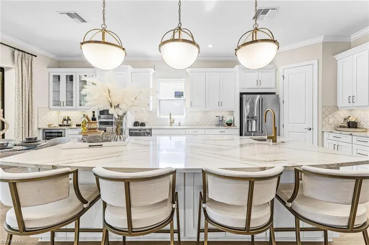 Kitchen with a kitchen bar, a large island with sink, decorative backsplash, white cabinetry, and decorative light fixtures