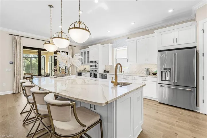 Kitchen featuring white cabinets, stainless steel appliances, tasteful backsplash, a large island with sink, and light stone counters
