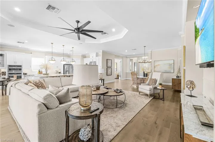 Living area with ceiling fan, light wood-type flooring, crown molding, suspended lighting, and a tray ceiling