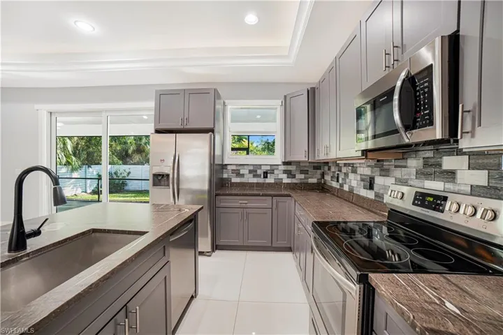 Kitchen with a raised ceiling, backsplash, sink, gray cabinetry, and stainless steel appliances