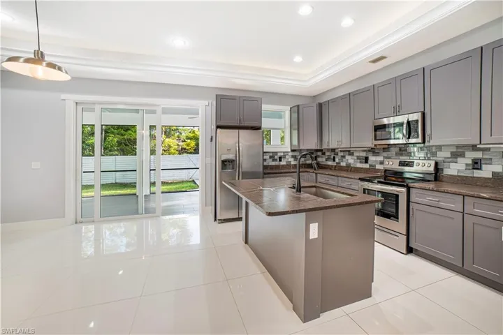 Kitchen featuring a kitchen island with sink, stainless steel appliances, backsplash, pendant lighting, and gray cabinets