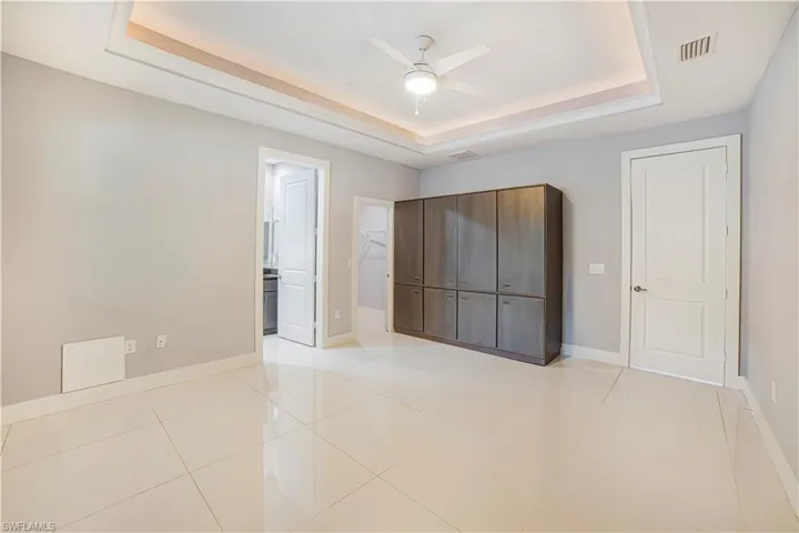 Unfurnished bedroom featuring ensuite bath, ceiling fan, light tile patterned floors, and a raised ceiling