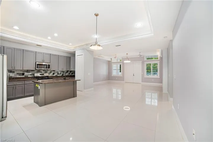 Kitchen featuring backsplash, appliances with stainless steel finishes, a raised ceiling, an island with sink, and pendant lighting