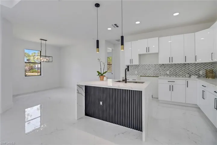 Kitchen with pendant lighting, sink, white cabinetry, and an island with sink
