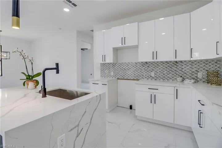 Kitchen featuring tasteful backsplash, light stone counters, sink, decorative light fixtures, and white cabinetry