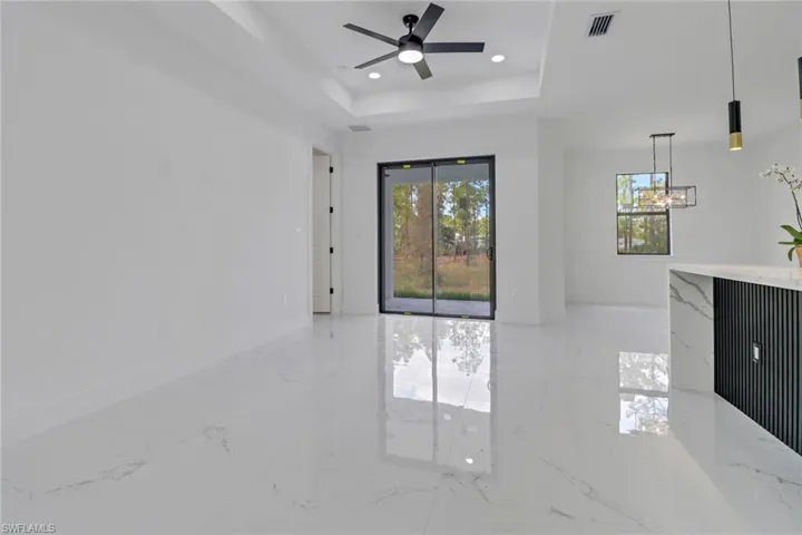 Unfurnished living room featuring a raised ceiling and ceiling fan with notable chandelier