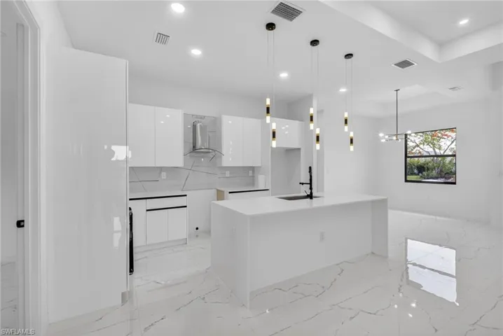 Modern kitchen featuring glossy white cabinetry, a spacious island with an integrated sink and black faucet, and contemporary pendant lighting