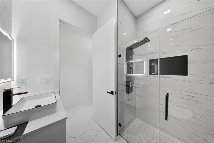 Contemporary bathroom with a frameless glass shower enclosure, a multi-function shower panel, and white marble-look wall and floor tiling