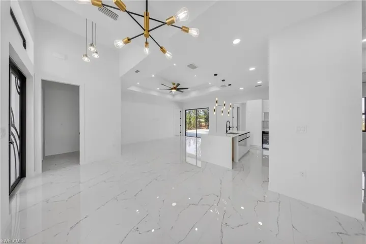 Spacious interior featuring high vaulted ceilings, large format white tile flooring with veining, and a modern kitchen island with pendant lighting