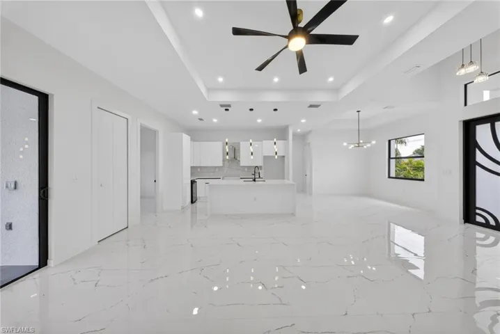 Open-concept living space featuring sleek white cabinetry, a kitchen island with sink, and white countertops