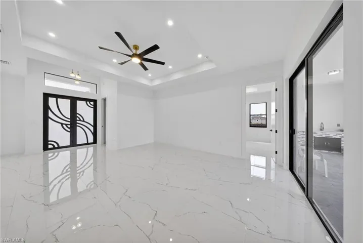 Spacious interior featuring marble-look tile flooring, a tray ceiling with recessed lighting, and a modern ceiling fan