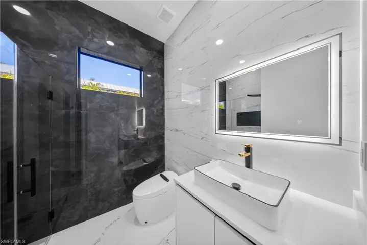 Modern bathroom featuring a rectangular vessel sink with a black and gold-tone faucet, a backlit vanity mirror, and recessed lighting