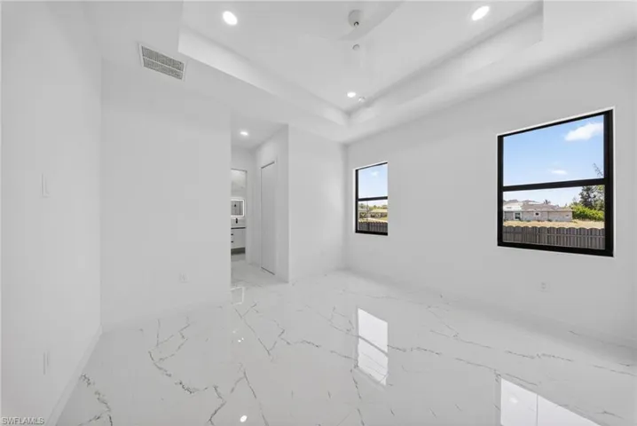 Spacious room featuring large format marble-look tile flooring, two windows with black frames, a tray ceiling, and recessed lighting