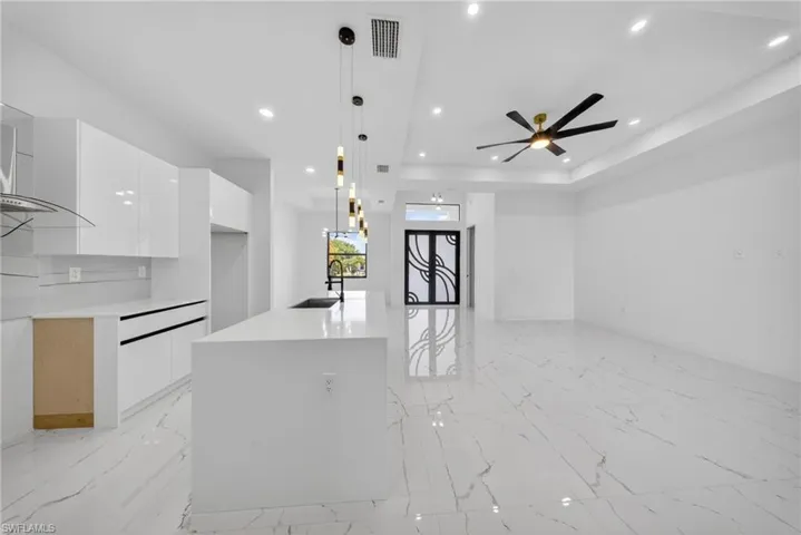 Open concept interior featuring large format marble-look tile flooring, a modern kitchen island with an undermount sink, recessed lighting, a contemporary ceiling fan, and an architectural front door