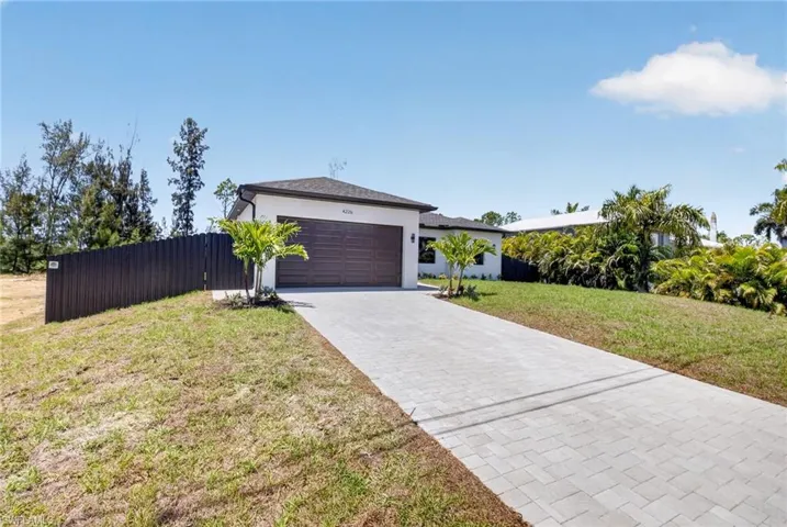 Contemporary single-story residence featuring a two-car garage with a wood-finish door, a light-colored stucco exterior, and a dark shingle roof
