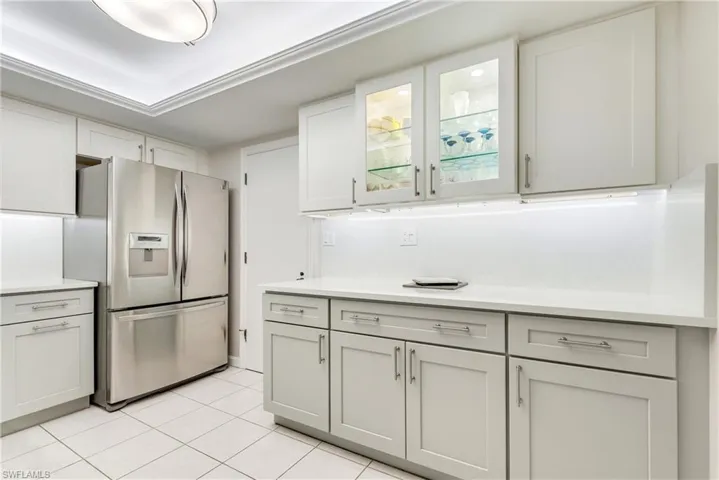 Kitchen featuring stainless steel refrigerator with ice dispenser, glass fronted cabinets, light tile patterned floors, light stone counters, and white cabinets