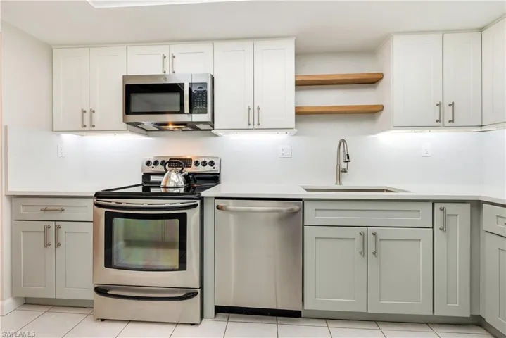 Kitchen with stainless steel appliances, open shelves, light tile patterned flooring, and light stone countertops