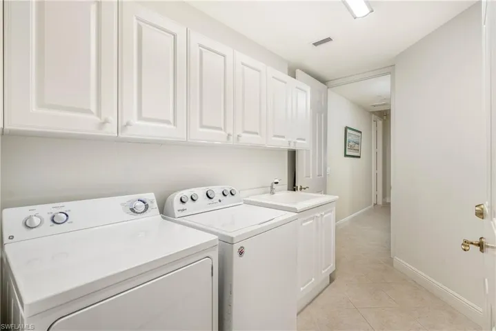 Laundry area with light tile patterned floors, washing machine and clothes dryer, and cabinet space