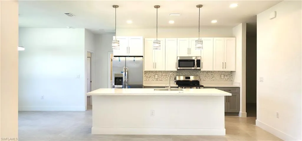 Kitchen with white cabinetry, decorative backsplash, an island with sink, pendant lighting, and appliances with stainless steel finishes
