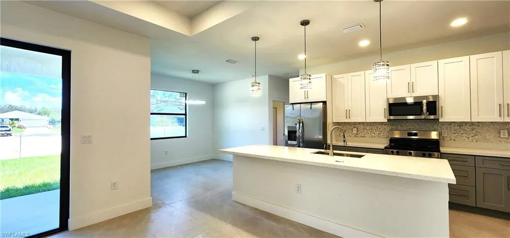 Kitchen with appliances with stainless steel finishes, a center island with sink, sink, backsplash, and light tile patterned floors