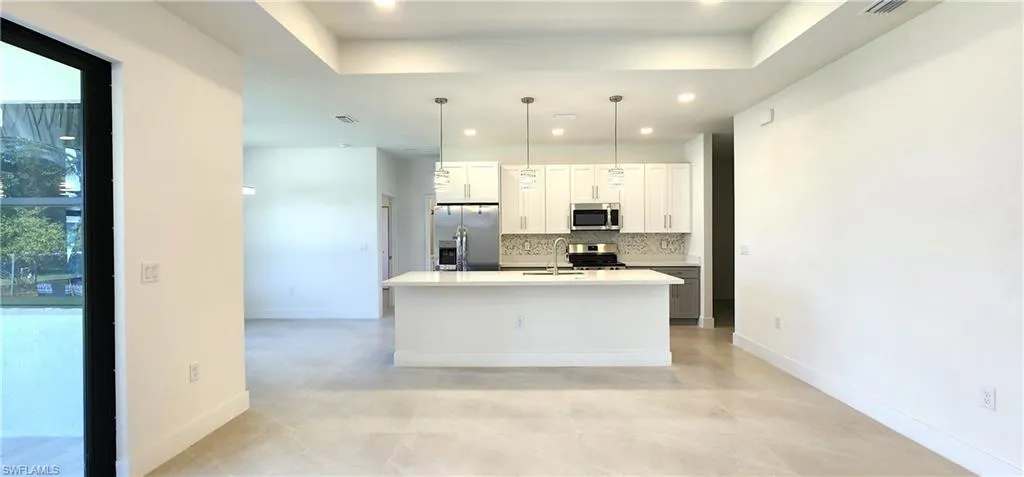 Kitchen featuring light tile patterned flooring, an island with sink, stainless steel appliances, decorative light fixtures, and a raised ceiling