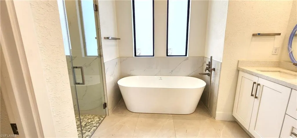Bathroom featuring vanity, plus walk in shower, tile walls, and tile patterned floors