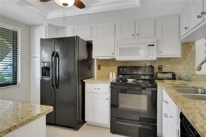 Kitchen featuring black appliances, white cabinetry, light stone countertops, a tray ceiling, and ornamental molding