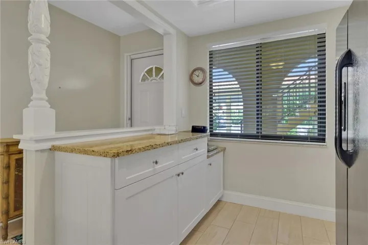 Kitchen featuring freestanding refrigerator, a peninsula, light stone countertops, and white cabinetry