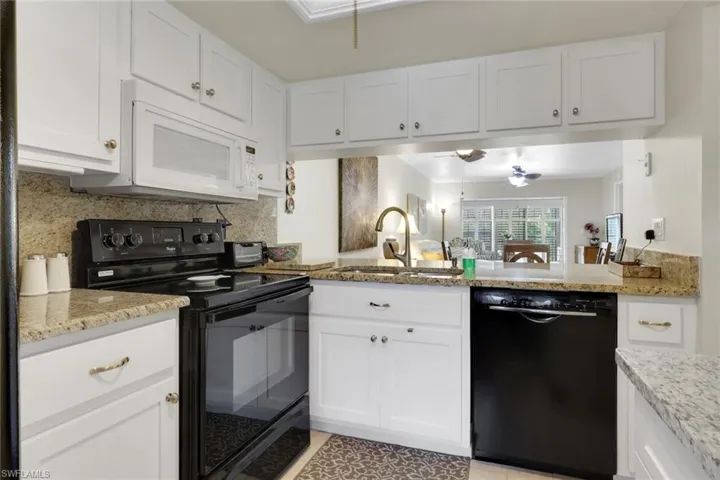 Kitchen with black appliances, white cabinets, decorative backsplash, and light stone counters