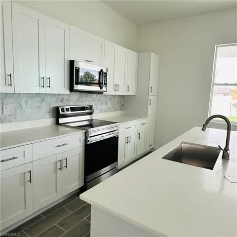 Kitchen with white cabinets, stainless steel appliances, decorative backsplash, wood tiled floors, and light stone counters