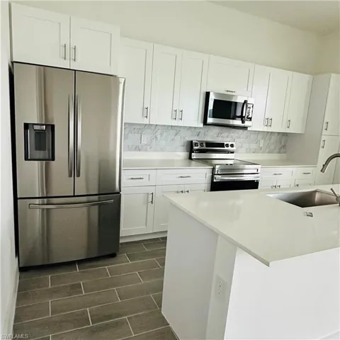 Kitchen with white cabinets, appliances with stainless steel finishes, backsplash, wood finish floors, and light stone countertops