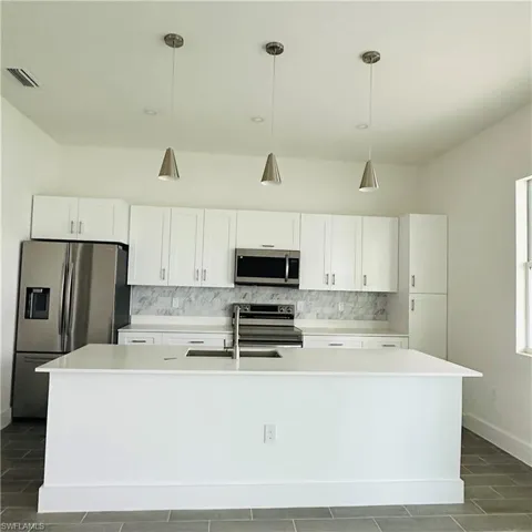 Kitchen with white cabinets, decorative backsplash, stainless steel appliances, hanging light fixtures, and a center island with sink