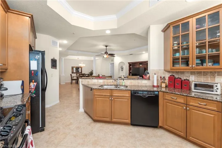 Kitchen with a peninsula, a sink, a raised ceiling, crown molding, and black appliances
