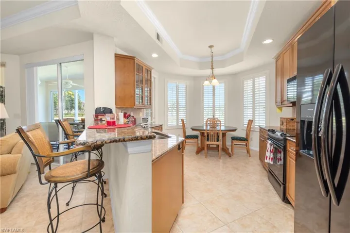 Kitchen featuring a kitchen breakfast bar, a tray ceiling, dark stone counters, black appliances, and glass insert cabinets