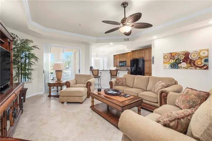 Living room featuring a tray ceiling, visible vents, a ceiling fan, ornamental molding, and light tile patterned floors