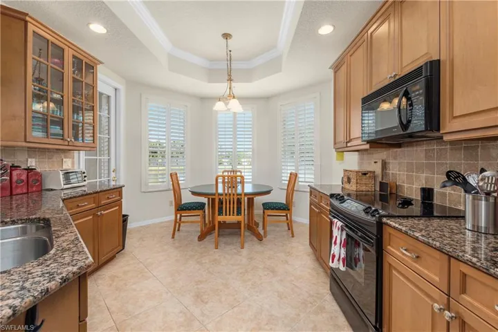 Kitchen with crown molding, tasteful backsplash, black appliances, a raised ceiling, and baseboards