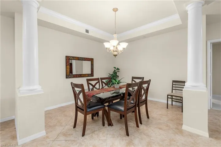 Dining room featuring a raised ceiling, ornamental molding, light tile patterned flooring, and ornate columns