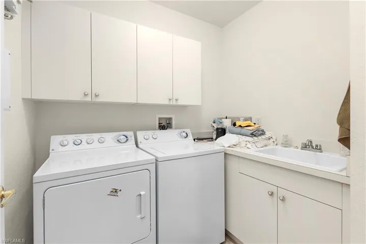 Washroom featuring washing machine and clothes dryer, cabinet space, and a sink