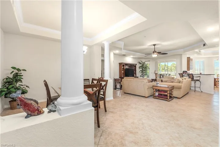 Living area with a tray ceiling, a ceiling fan, light tile patterned floors, crown molding, and decorative columns
