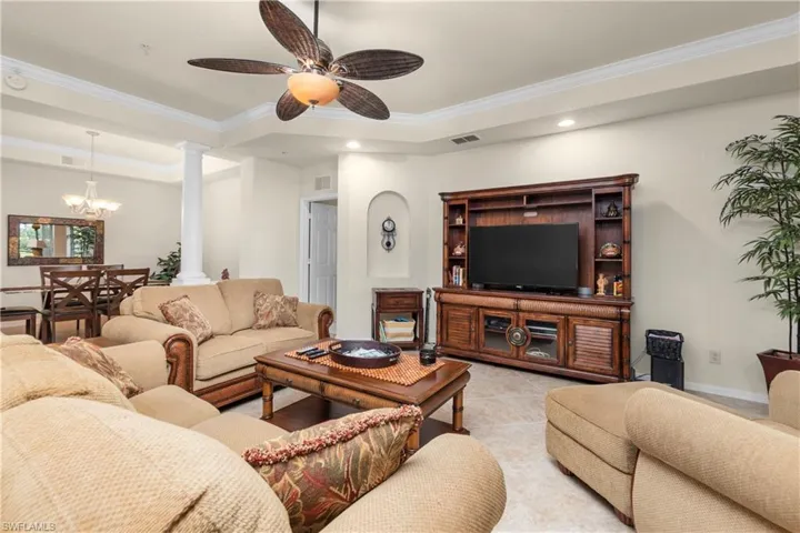 Living room featuring crown molding, ceiling fan with notable chandelier, ornate columns, a raised ceiling, and recessed lighting